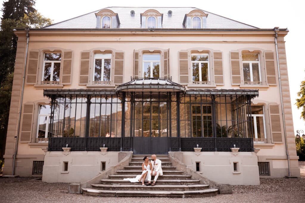 Couple de mariés assis sur les marches du manoir de la Villa des Hêtres Pourpres.