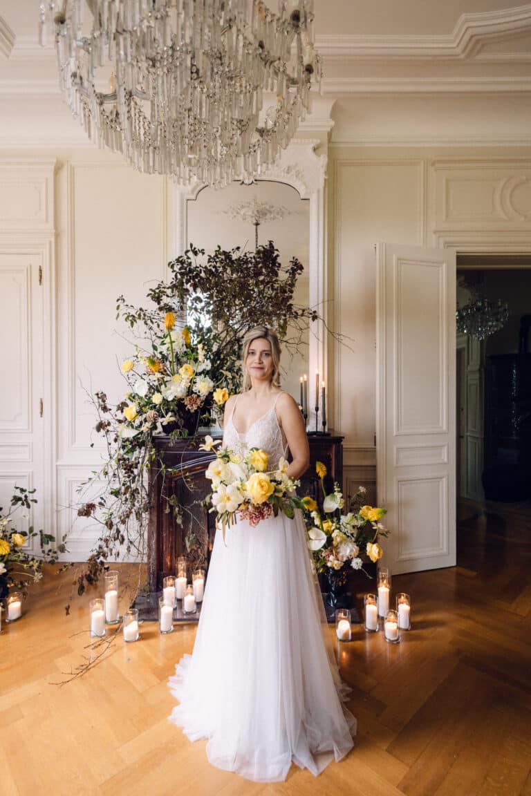 Mariée posant dans une salle décorée de fleurs jaunes et de bougies.