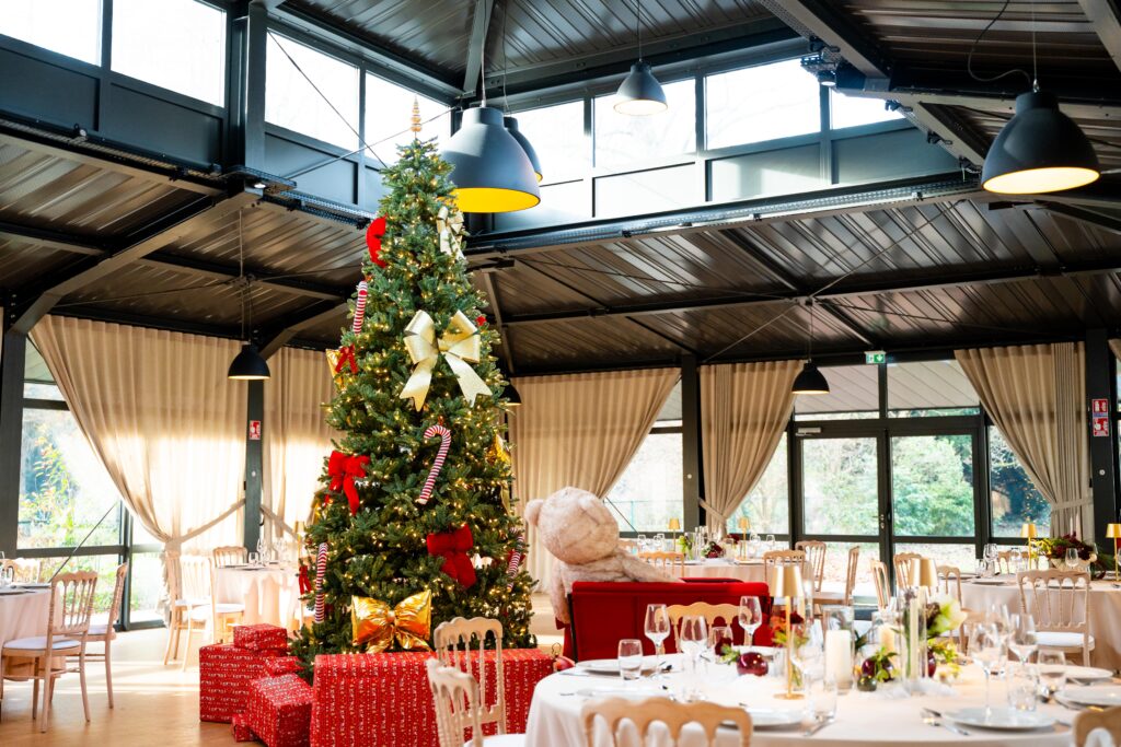 DSC00646 – La villa des hêtres pourpres Christmas tree centerpiece with gold bows and candy canes in a bright dining hall, surrounded by wrapped presents and set tables.