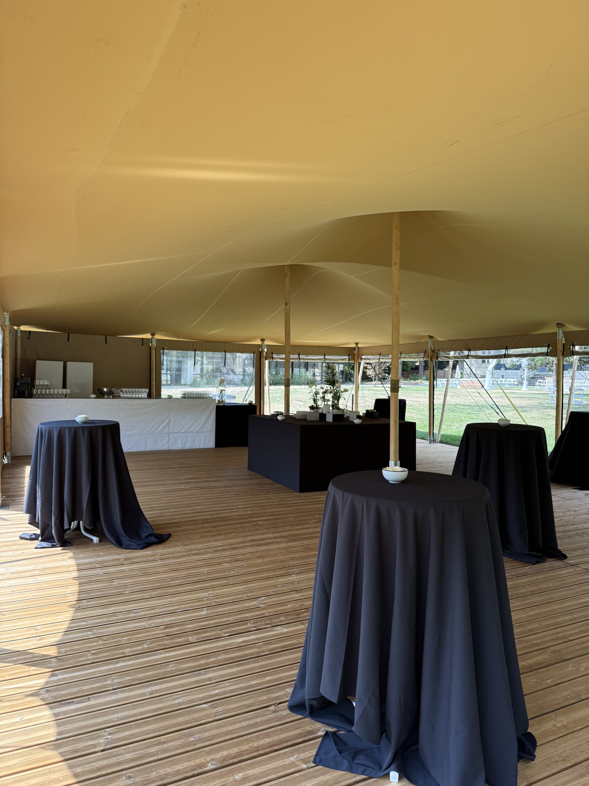 IMG_7219 – La villa des hêtres pourpres Indoor event tent with beige ceiling and round tables covered in black cloth on a wooden deck